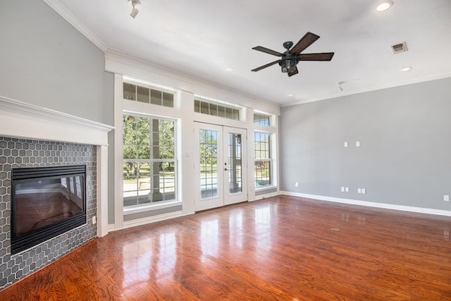 unfurnished living room featuring a fireplace, hardwood / wood-style floors, ornamental molding, ceiling fan, and french doors