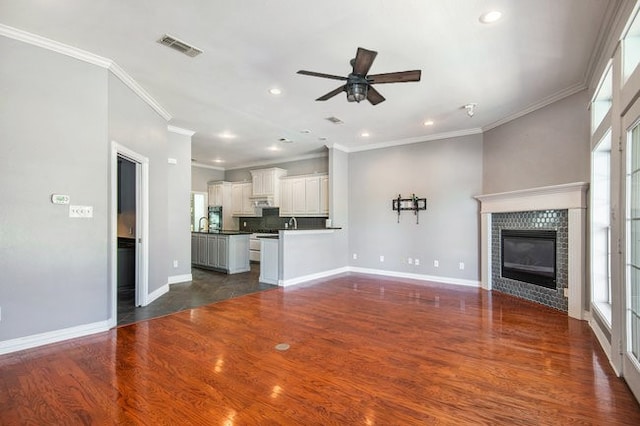 unfurnished living room with ceiling fan, dark hardwood / wood-style floors, ornamental molding, and a tile fireplace