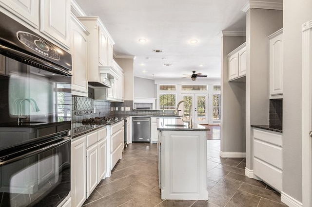 kitchen featuring white cabinetry, an island with sink, tasteful backsplash, ceiling fan, and stainless steel dishwasher