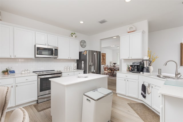 kitchen with light hardwood / wood-style flooring, white cabinetry, stainless steel appliances, a center island, and decorative backsplash