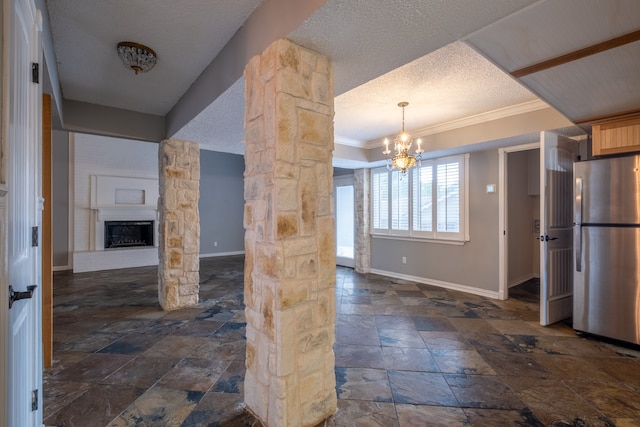 kitchen featuring stainless steel fridge, a fireplace, crown molding, an inviting chandelier, and decorative columns