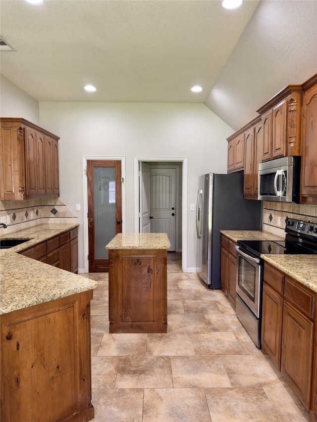 kitchen featuring vaulted ceiling, a kitchen island, decorative backsplash, appliances with stainless steel finishes, and light stone countertops