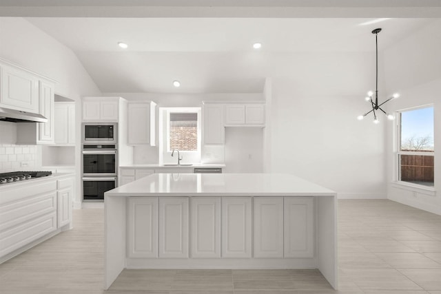 kitchen featuring appliances with stainless steel finishes, decorative light fixtures, white cabinetry, sink, and a center island