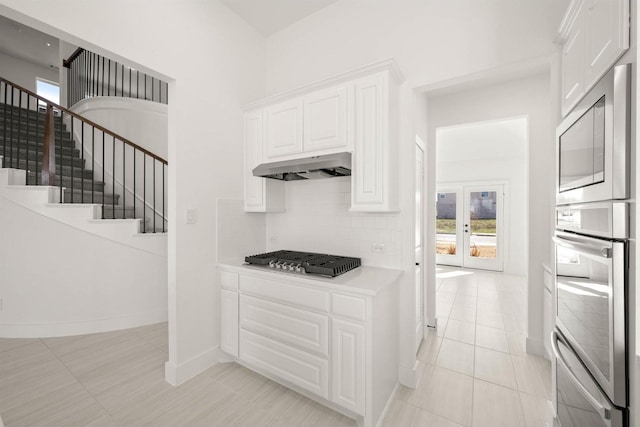 kitchen with light tile patterned floors, stainless steel appliances, a wealth of natural light, white cabinets, and decorative backsplash