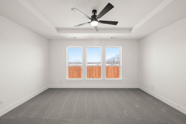 empty room with a tray ceiling, ceiling fan, and carpet