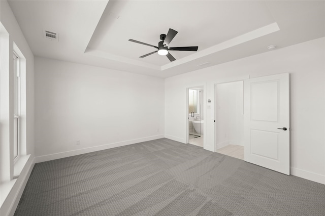 unfurnished bedroom with a tray ceiling, light colored carpet, and ensuite bathroom