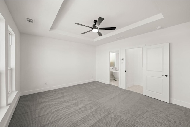 unfurnished bedroom featuring ceiling fan, light colored carpet, a tray ceiling, and ensuite bath