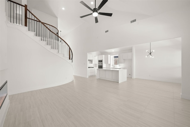 unfurnished living room with a towering ceiling, sink, and ceiling fan with notable chandelier