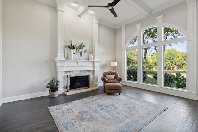 living area featuring beamed ceiling, a healthy amount of sunlight, a stone fireplace, and dark hardwood / wood-style floors