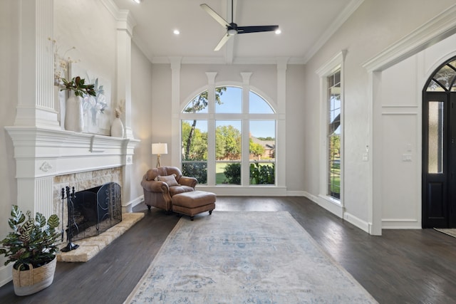 sitting room featuring a high ceiling, ceiling fan, dark wood-type flooring, a stone fireplace, and ornamental molding