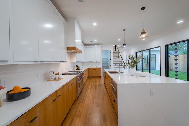 kitchen featuring white cabinetry, sink, double oven range, decorative light fixtures, and light hardwood / wood-style flooring