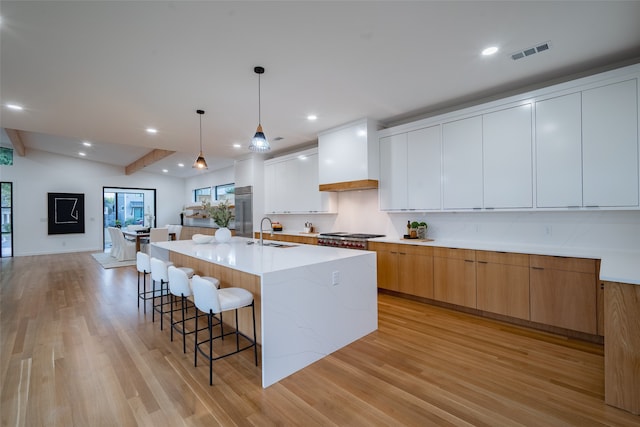 kitchen with white cabinets, hanging light fixtures, sink, a large island, and light wood-type flooring