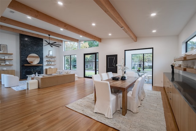 dining area with lofted ceiling with beams, ceiling fan, a large fireplace, and light hardwood / wood-style flooring