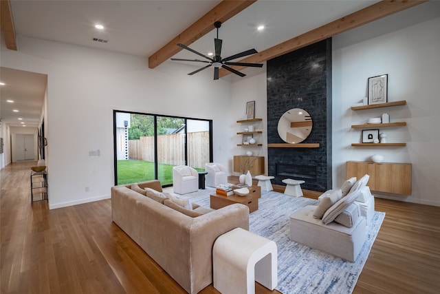 living room with a brick fireplace, hardwood / wood-style flooring, ceiling fan, beam ceiling, and a high ceiling