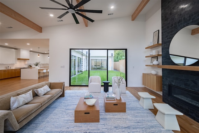 living room featuring a fireplace, beamed ceiling, light hardwood / wood-style flooring, and high vaulted ceiling