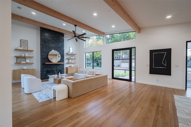 living room featuring ceiling fan, beam ceiling, a fireplace, a towering ceiling, and light wood-type flooring