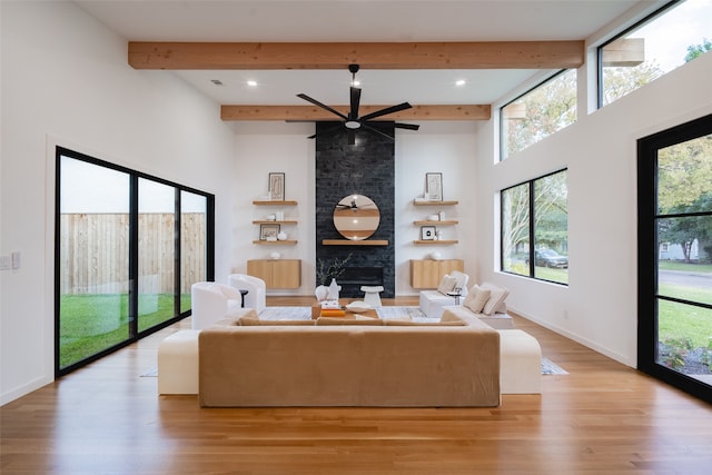 living room with beam ceiling, light wood-type flooring, a wealth of natural light, and a large fireplace