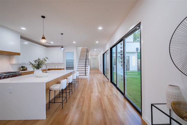 kitchen with light stone counters, white cabinets, hanging light fixtures, a kitchen island with sink, and light hardwood / wood-style flooring