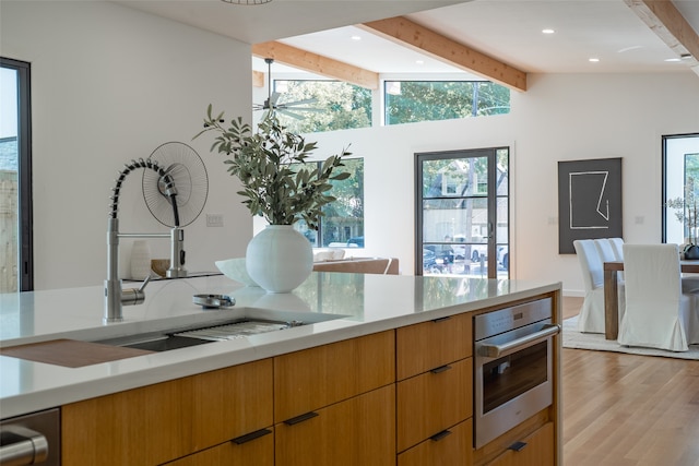 kitchen with ceiling fan, vaulted ceiling with beams, sink, oven, and light hardwood / wood-style floors