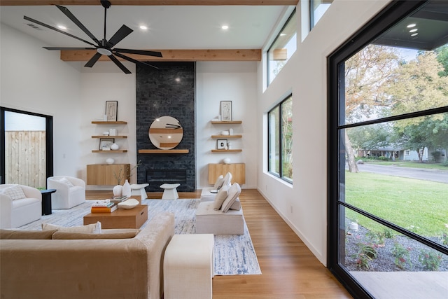 living room featuring ceiling fan, light wood-type flooring, a high ceiling, and a large fireplace