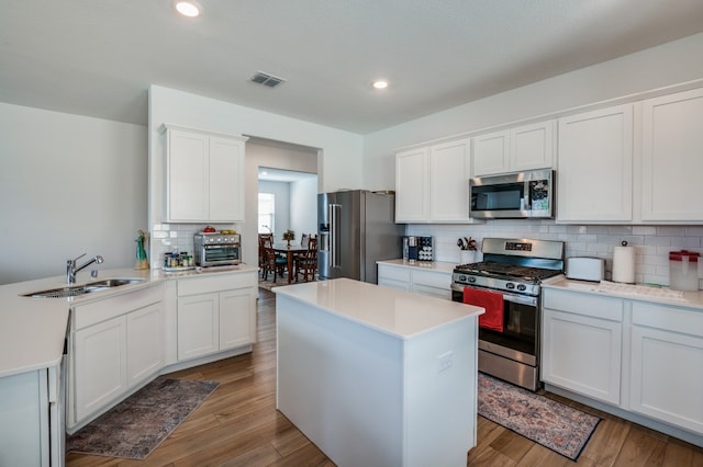 kitchen with appliances with stainless steel finishes, light hardwood / wood-style floors, white cabinets, backsplash, and sink