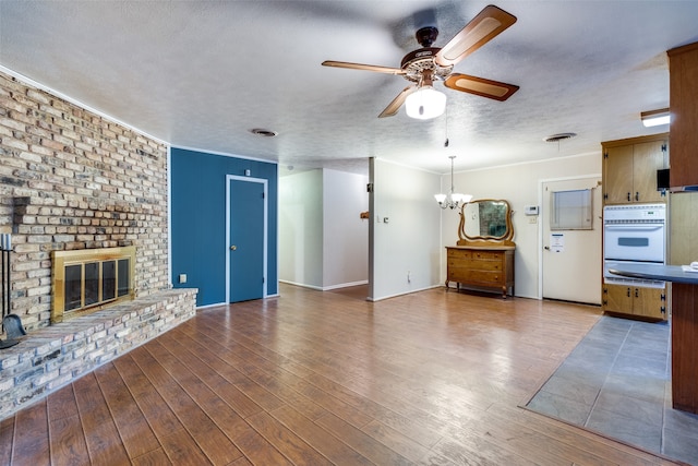 unfurnished living room with a brick fireplace, ceiling fan with notable chandelier, a textured ceiling, wood-type flooring, and crown molding