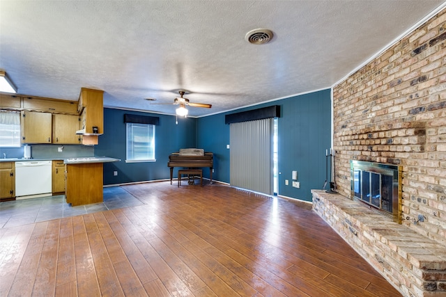 kitchen featuring a brick fireplace, dishwasher, a textured ceiling, wood-type flooring, and crown molding