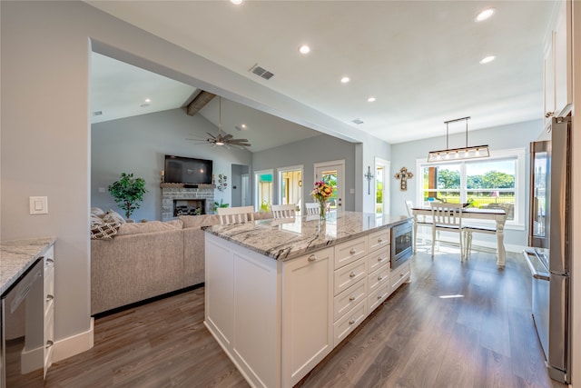 kitchen with appliances with stainless steel finishes, white cabinetry, a brick fireplace, a kitchen island, and vaulted ceiling with beams