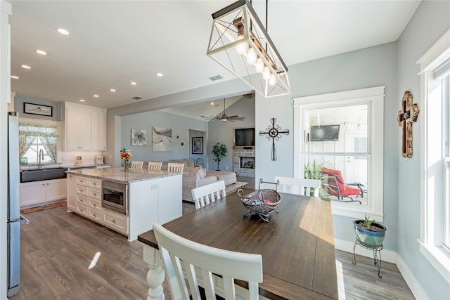 dining room with ceiling fan, dark wood-type flooring, a fireplace, and sink