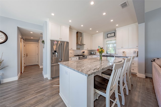 kitchen with hardwood / wood-style flooring, stainless steel appliances, wall chimney exhaust hood, and a kitchen island