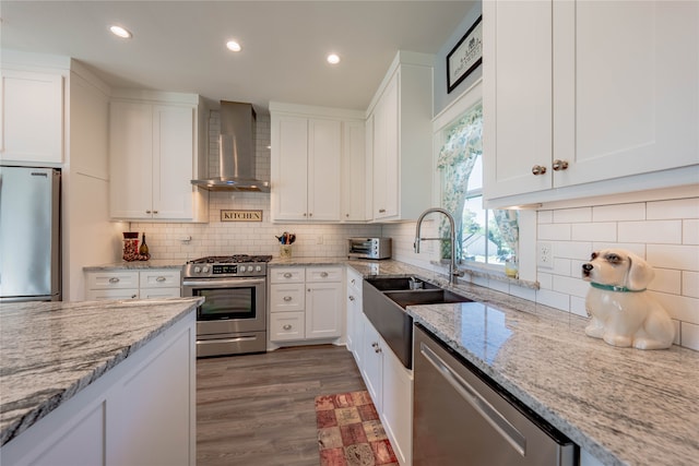 kitchen featuring light stone countertops, white cabinetry, appliances with stainless steel finishes, and wall chimney range hood