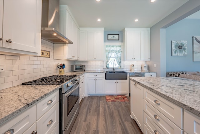 kitchen with dark wood-type flooring, wall chimney range hood, high end stainless steel range, and white cabinets