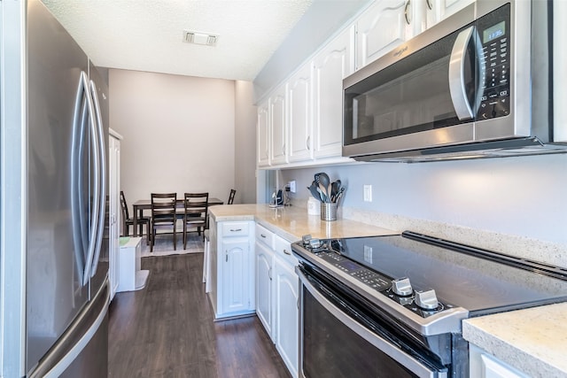 kitchen featuring dark hardwood / wood-style floors, appliances with stainless steel finishes, white cabinetry, and a textured ceiling