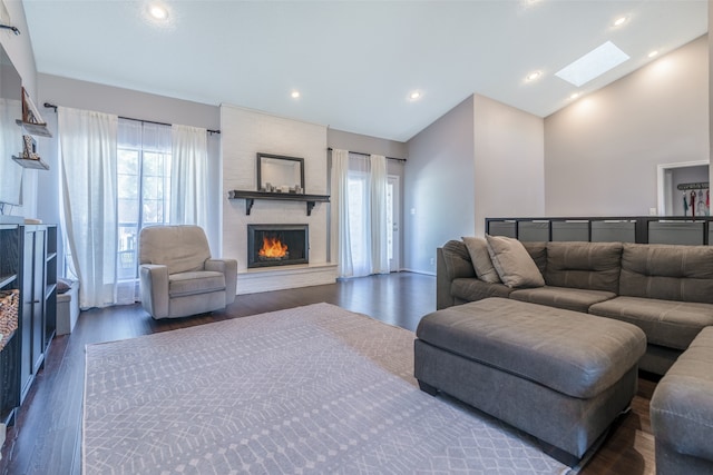 living room featuring a skylight, a fireplace, dark wood-type flooring, and high vaulted ceiling