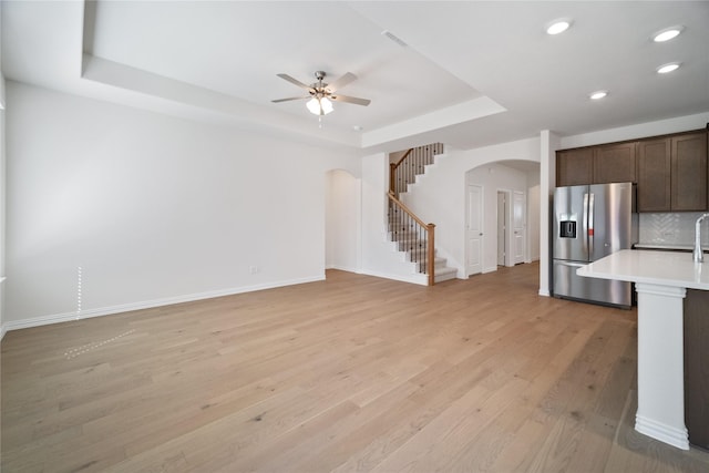 unfurnished living room with arched walkways, light wood-style flooring, baseboards, stairs, and a raised ceiling