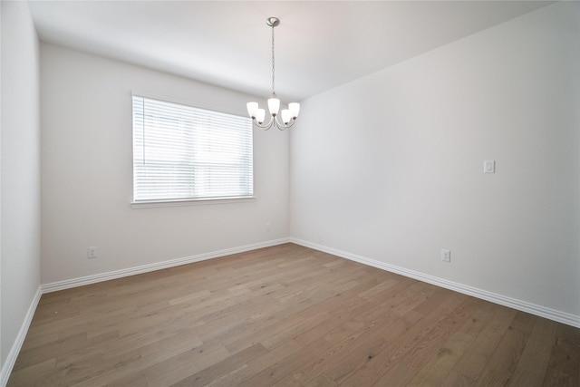 empty room with a chandelier, baseboards, and wood finished floors