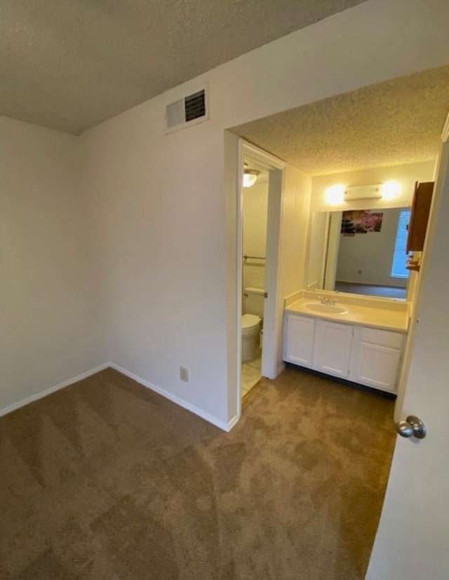 unfurnished bedroom featuring a textured ceiling, connected bathroom, carpet flooring, and sink