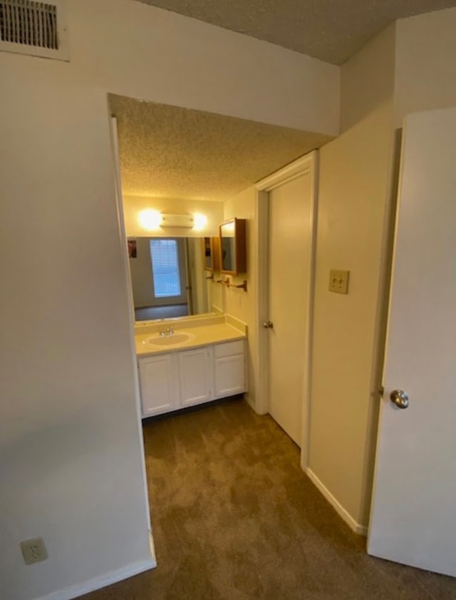 hallway with dark colored carpet, a textured ceiling, and sink