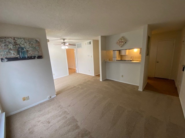 unfurnished living room featuring ceiling fan, light colored carpet, and a textured ceiling