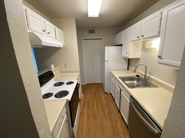 kitchen featuring wood-type flooring, a textured ceiling, sink, white cabinetry, and white appliances