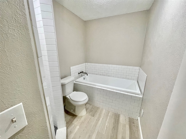 bathroom with hardwood / wood-style floors, a textured ceiling, a relaxing tiled tub, and toilet