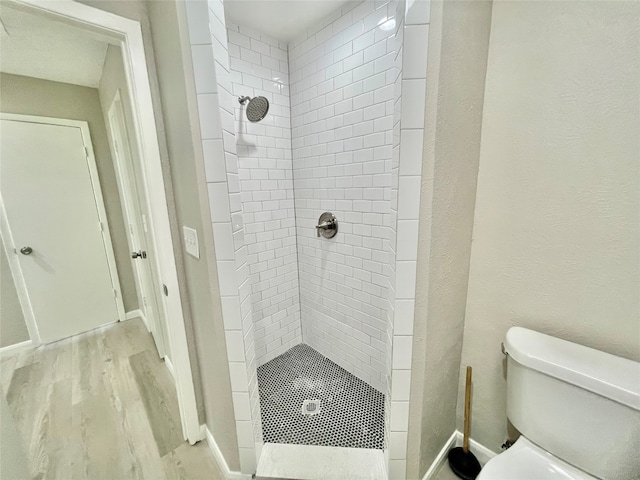 bathroom featuring toilet, a tile shower, and hardwood / wood-style flooring