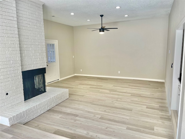 unfurnished living room with a textured ceiling, ceiling fan, and a brick fireplace