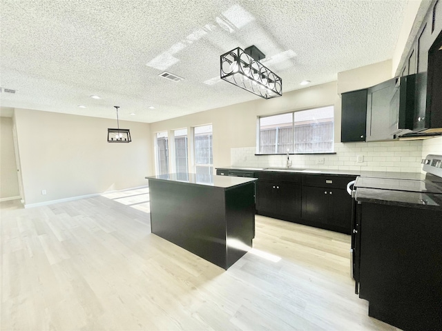 kitchen featuring sink, a kitchen island, decorative light fixtures, light wood-type flooring, and decorative backsplash