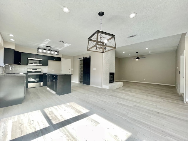 kitchen featuring a barn door, pendant lighting, stainless steel appliances, light wood-type flooring, and ceiling fan