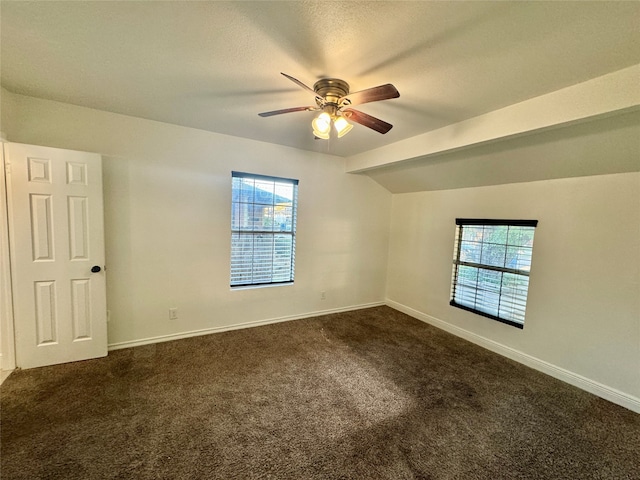 unfurnished room featuring a healthy amount of sunlight, lofted ceiling, dark colored carpet, and ceiling fan