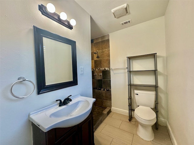 bathroom featuring tile patterned flooring, tiled shower, vanity, and toilet