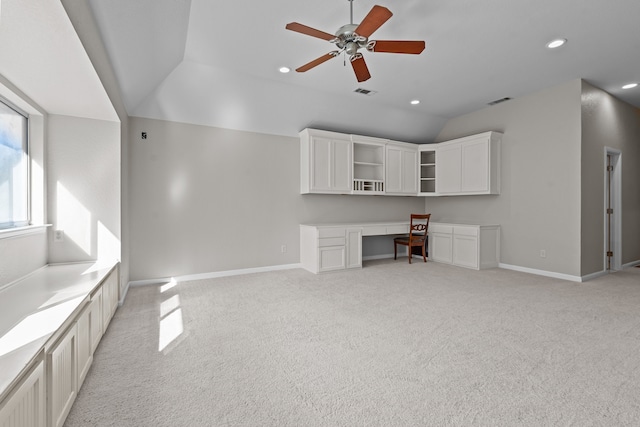 unfurnished living room with ceiling fan, built in desk, light carpet, and vaulted ceiling