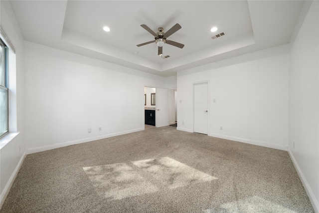 carpeted spare room featuring a tray ceiling, ceiling fan, and plenty of natural light