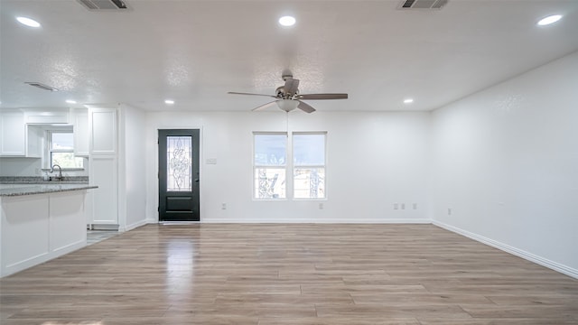 unfurnished living room featuring ceiling fan, light wood-type flooring, sink, and a wealth of natural light